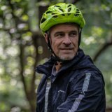 Ein Mann mit Fahrradhelm und teils nasser Regenjacke.