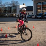 Eine Person fährt auf einem Platz mit einem E-Bike zwischen orangefarbenen Pylonen.