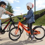 Zwei unterschiedlich große Kinder stehen mit Fahrrädern auf einem Platz und reden miteinander.