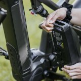 Eine Person hält einen Akku neben ein E-Bike.