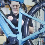Ein Mann hantiert in einer Werkstatt an einem Kabel, dass an einem E-Bike angeschlossen ist.
