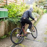 Eine Person mit Kapuze steigt zwischen Briefkästen und einer Hauswand auf ein Fahrrad, um loszufahren.