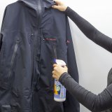 Eine Frau besprüht eine Jacke mit Imprägnierung aus einer Pumpsprühflasche.