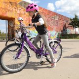 Ein Mädchen setzt an, mit dem Fahrrad loszufahren. Im Hintergrund fährt ein anderes Kind.