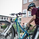 Ein Kind nimmt das Schloss von der Sattelstütze eines blauen Fahrrades in einem Fahrradständer.