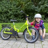 Ein Kind sitzt neben einem grünen Kinderrad auf einer Bordsteinkante.