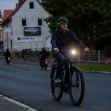 Ein Mann fährt in der Dämmerung mit dem Fahrrad auf einer Straße. Sehr deutlich zu sehen ist der leuchtende Frontscheinwerfer.