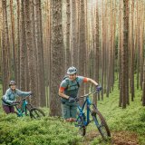 Eine Frau und ein Mann schieben ihre Mountainbikes im Wald einen Weg bergan.