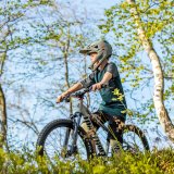 Ein Kind mit Fullface-Helm und einem Mountainbike zwischen Bäumen.