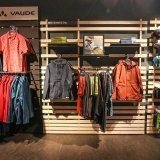 Eine Produktpräsentationswand mit Jacken, Oberteilen und Taschen der Firma Vaude.