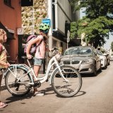 Ein Mädchen mit und eins ohne Fahrrad stehen am Straßenrand und schauen nach Autos, bevor sie die Straße überqueren.