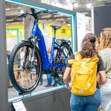 Mehrere Personen betrachten ein blaues E-Bike an einem Messestand.