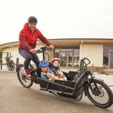 Ein Mann fährt ein Lastenrad mit zwei Kindern.