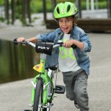 Ein Kind mit grünem Helm schiebt ein grünes Fahrrad.