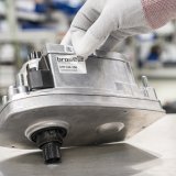 Eine Person klebt einen Aufkleber mit dem Logo der Firma Brose und einigen Codierungen auf eine E-Bike-Antriebseinheit.