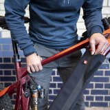 Eine Person wickelt eine Schutzhülle mit Klettverschluss um das Unterrohr und damit den Akku eines E-Bikes.