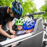 Ein Mann schnallt zwei Kinder in einem Lastenrad an.