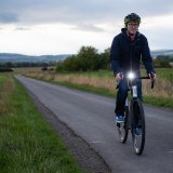 Ein Mann fährt in der Dämmerung eine schmale Landstraße mit einem beleuchteten Fahrrad entlang.