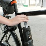 Ein Person verstaut einen länglichen Gegenstand in einer Transportbox, die ähnlich einer Trinkflasche am Fahrradrahmen angebracht ist.