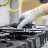 Die Hand einer Person, die ein Bauteil aus einer Verpackung auf einem Tisch nimmt.