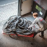 Ein Mann schiebt einen Fahrradanhänger mit alten Fahrradreifen aus einem Tor heraus.