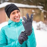 Eine lachende Frau zieht sich in verschneiter Umgebung Handschuhe an.