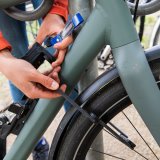 Detailaufnahme einer Person, die mit einem Faltschloss das Vorderrad und den Rahmen eines Fahrrads an einem Fahrradständer anschließt.