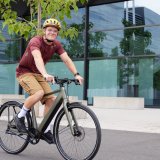 Ein Mann fährt auf einem E-Bike vor einem Gebäude mit Glasfassade entlang.