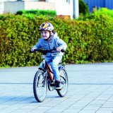 Ein Kind mit buntem Helm fährt mit einem Fahrrad über einen Platz.