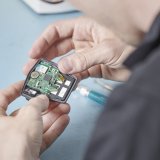 Blick über die Schulter einer Person, die ein offenes elektronisches Bauteil in den Händen hält.