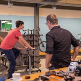 Eine Person sitzt in einem Fahrradladen auf einem Ergometer. Eine zweite Person schaut von der Seite darauf.