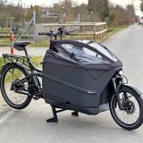 Ein Lastenrad mit verkleidetem Laderaum auf einer Fahrbahn.