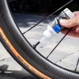 Eine Person füllt eine Flüssigkeit aus einer Kunststoffflasche in das Ventil eines Rennrades.