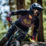 Frau mit Helm und Brille fährt mit Mountainbike durch Wald 