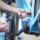 Die Hände einer Person, die ein Ladekabel am Rahmen eines E-Bikes anschließt oder abzieht.