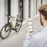 Blick über die Schulter eines Mannes, der auf ein Smartphone schaut. Im Hintergrund steht ein E-Bike vor einem Gebäude.