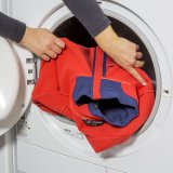 Eine Person steckt eine Jacke in eine Waschmaschine.