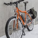 Ein orangefarbenes E-Bike mit Schnee in den Rädern und am Rahmen steht an eine Wand gelehnt.