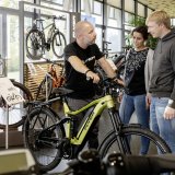 Ein Mann steht mit einem E-Bike in einem Fahrradladen und unterhält sich mit einer Frau und einem Mann.