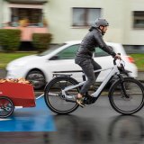 Ein Mann fährt auf einer Fahrradstraße mit einem E-Bike durch ein Wohngebiet. Am Rad hängt ein roter Anhänger.