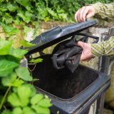 Eine Person wirft einen zusammengeknüllten Fahrradschlauch in eine Mülltonne.