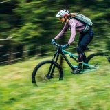 Eine Frau fährt auf einem Mountainbike einen Wiesenweg bergab.