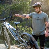 Ein Mann steht in der Natur neben einem E-Bike und betrachtet es.