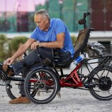 Ein Mann fixiert seine Schuhe auf dem Pedal eines Liegedreirads.