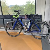 Ein blaues Fahrrad lehnt in einem Zug an Klappsitzen. Am Lenker hängt ein Helm.