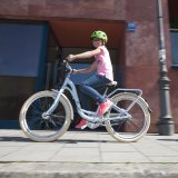 Ein Kind fährt mit einem Fahrrad auf einem Fußweg vor einem Gebäude.