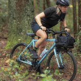 Eine Frau fährt auf einem blauen Fahrrad durch den Wald.