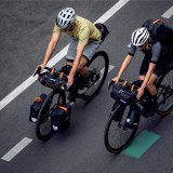 Draufsicht auf zwei Personen, die auf Fahrrädern mit Gepäck auf einer Straße fahren.