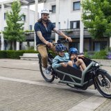 Ein Mann transportiert zwei Kinder in einem Lastenrad.