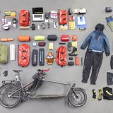 Auf dem Boden übersichtlich ausgebreitetes Gepäck und Ausrüstung sowie ein Lastenrad.